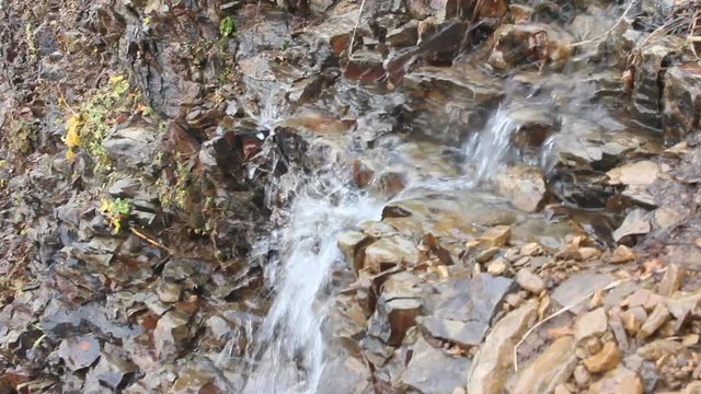 Small waterfall on cliff to sea. Strong wind rips water and throws it back
