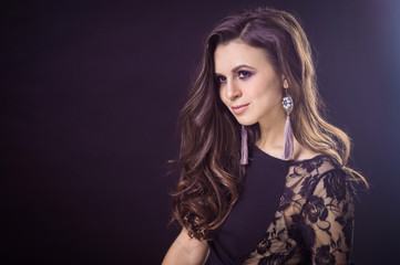 Naklejka premium Beautiful brunette girl with flowing hair on a dark background and in earrings