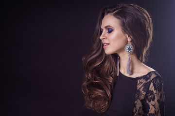 Beautiful brunette girl with flowing hair on a dark background and in earrings