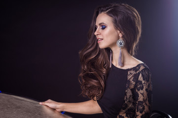 Fototapeta premium Beautiful brunette girl with flowing hair on a dark background and in earrings
