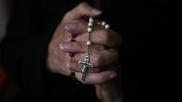 closeup of old woman&rsquo;s hands praying and holding a rosary
