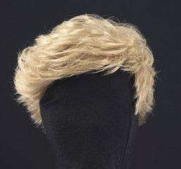 blonde feminine wig on black background and textile mannequin. - obrazy, fototapety, plakaty