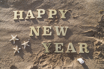 Happy New Year/Happy New Year wood sign, starfish and shellfish on the sandy beach.
