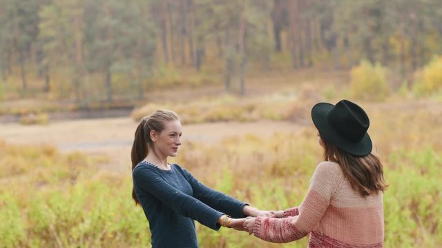 Two beutiful girls dancing in the autumn forest and have fun. They laughing and spin around