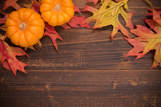 Autumn leaves  and pumpkins on a wooden background forming a bor