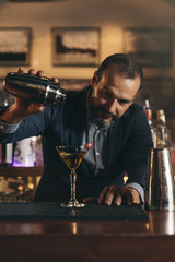Barman is making cocktail at night club.
