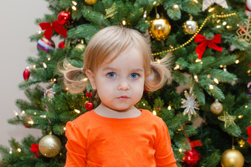 Toddler girl on the Christmas tree background. Child in holiday decorated living room.
