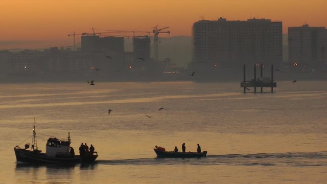 silhouette of a small boat travelling on the water with urban tangier city skyline in the background.