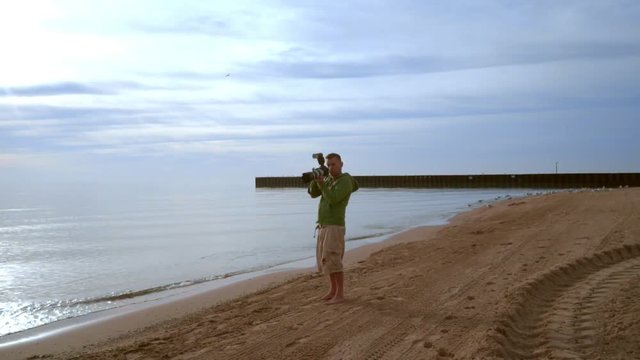 Photographer with camera on sea beach. Photographer shooting with professional camera. Photographer beach. Professional camera with big camera lens. Photographer shooting outdoor