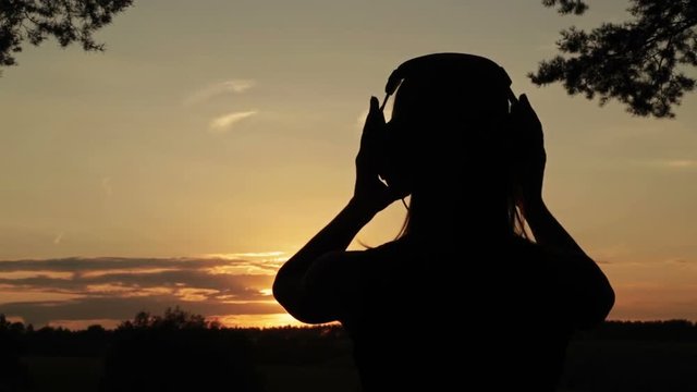 Woman putting on the headphones, listening to music and dancing in the forest. Sunset light, sun lens flares, golden hour. Relax, nature and joyful concept
