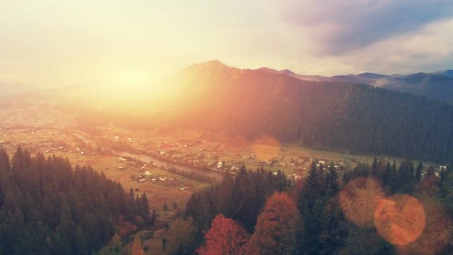 Aerial Drone Footage View: Flight over autumn mountain village with forest in sunrise soft light. Image processed in orange glow. Carpathian Mountains, Ukraine, Europe. Majestic landscape. Beauty