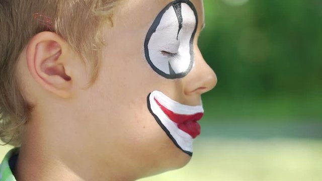 professional artist apply make-up clown on the face of a child close up outdoors