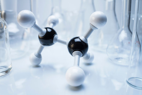 Ball and stick molecular model of ethane, surrounded by laboratory flasks