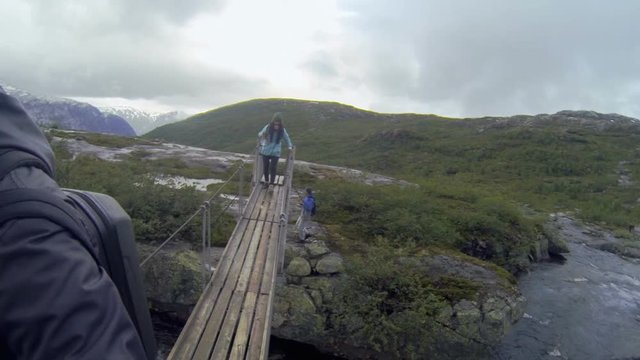 Norway. The girl and two guys go over the bridge across mountain river