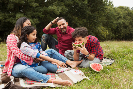 Family sitting outdoors, on picnic blanket, son eating watermelon