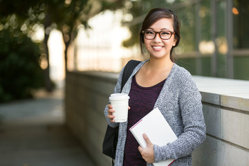 Asian american university student smiling with coffee and book bag on campus with print space
