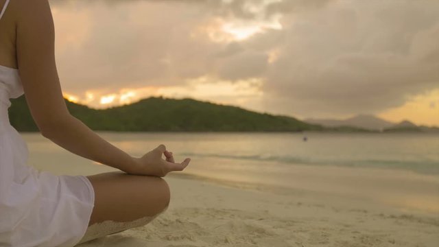 woman doing yoga meditation on tropical beach at sunset