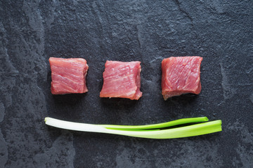 Three cubes of meat and green onions on the black table