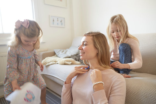 Girl putting necklace onto mother in living room