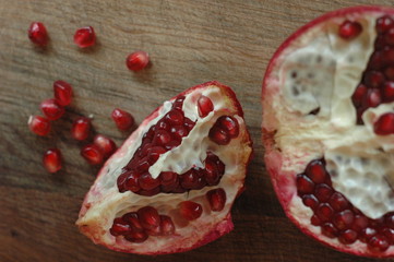 Have broken pomegranates and several garnet berries on a wooden surface.