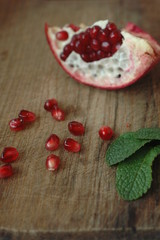 Have broken pomegranates and several garnet berries on a wooden surface.