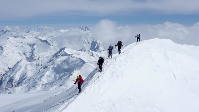 a mountain guide and clients on an exposed summit ridge during a winter ascent in the Austrian Alps