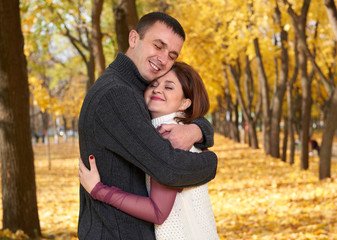 Fototapeta premium romantic people, happy adult couple embrace in autumn city park, trees with yellow leaves, bright sun and happy emotions, tenderness and feelings