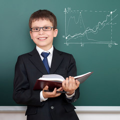 school boy with book, chart drawing on chalkboard background, dressed in classic black suit, education concept