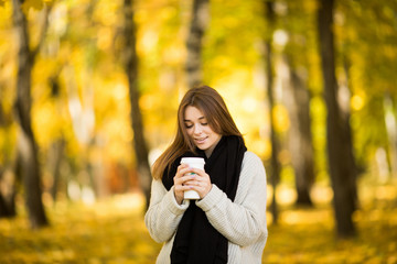 Young girl drink coffee in autumn yellow  sunny park
