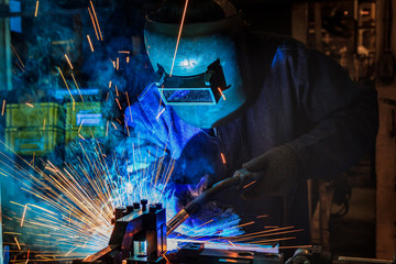 worker is welding automotive part in factory with protective mask and bright sparks.