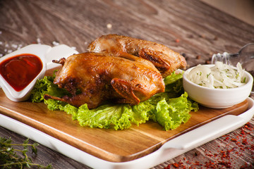 Quails grilled on a wooden board and a white plate, spilling aro