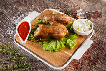 Quails grilled on a wooden board and a white plate, spilling aro