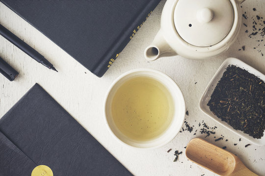 cup with green tea, book and teapot on white wooden table background. over light and old film color tone