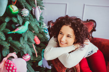 beautiful and young woman with curly hair sits near Christmas tr