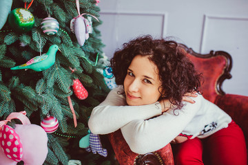 beautiful and young woman with curly hair sits near Christmas tr