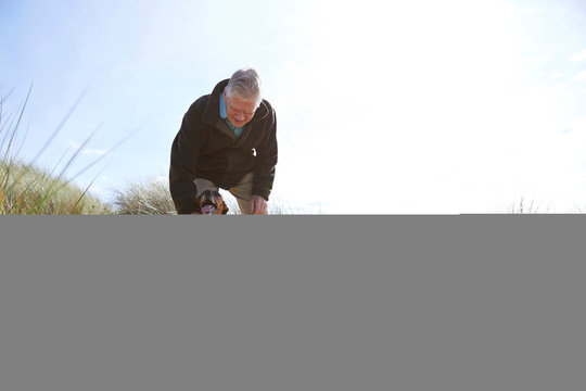 Man stroking pet dog on sand dunes, Constantine Bay, Cornwall, UK