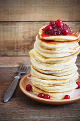 Stack of delicious pancakes with cranberries on plate and napkin wooden background
