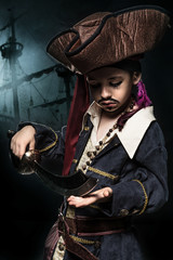 Fototapeta premium A angry young boy wearing a pirate costume. He stands on the background of the ship