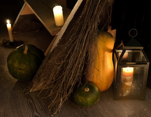 Scary occult still life with witch broomstick, pumpkins and candles by staircase