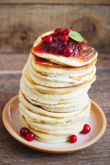 Stack of delicious pancakes with cranberries on plate and napkin wooden background