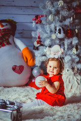The small girl sits near christmas tree