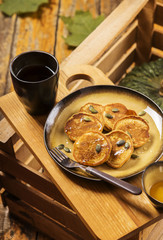 Pumpkin pancakes topped with honey and sprinkled with pumpkin seeds on a plate with the effect of craquelure on a wooden box with a cup of tea and a bowl with honey. Selective focus 