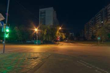 unpopulated night intersection with traffic lights and pedestrian crossings. against the backdrop of lights, trees and houses, street of the city of Novosibirsk