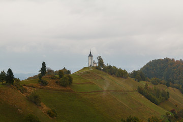 Jamnik church on a hillside in autumn, foggy weather at sunset in Slovenia