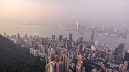 Beautiful aerial shot of many high skyscrapers covered with sunset fog or haze in Hong Kong, China. Top view of Victoria Harbour from Victoria Peak at sunset. City skyline.