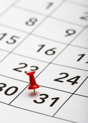Pin on the date number 31. The thirty first day of the month is marked with a red thumbtack. Last day of month. Focus point on the red pin.