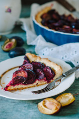 Homemade pie with plums on the blue wooden background table. Baked and raw plums.