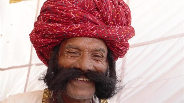 Smiling man from Rajasthan salutes with big moustache wearing a red turban and tradition dress