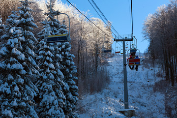 Winter mountain lift for skiers above snowy forest and sky