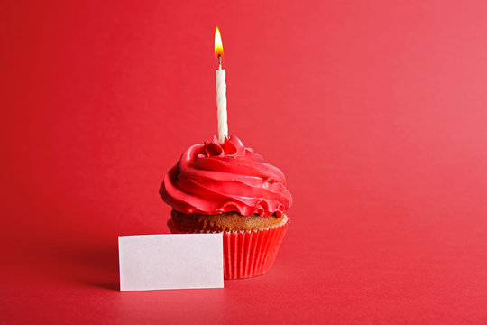Fresh tasty cupcake with candle and birthday card on red background